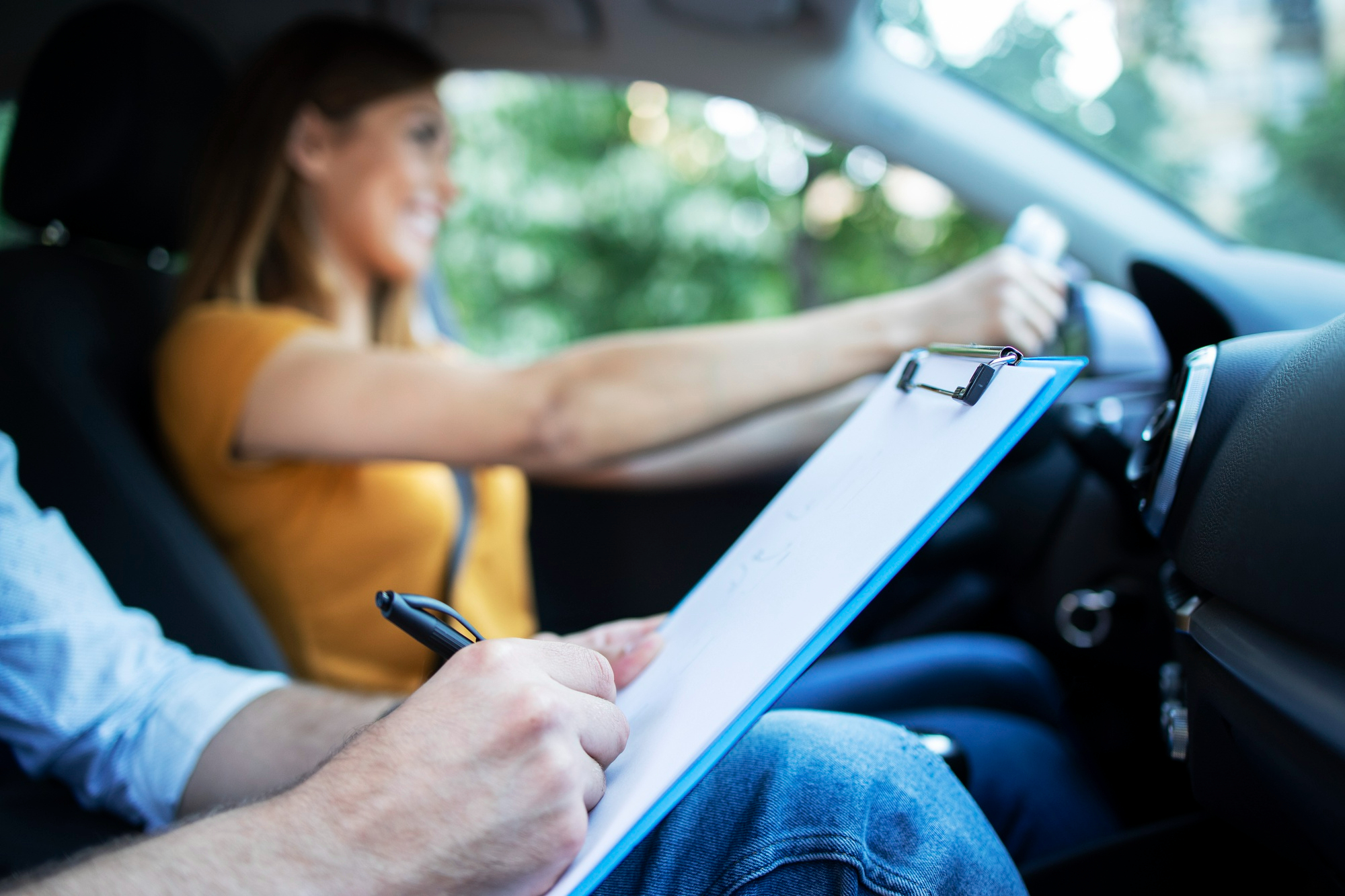 close-up-view-driving-instructor-holding-checklist-while-background-female-student-steering-driving-car